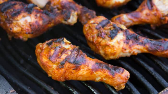 Chicken drumsticks cooking on a grill.