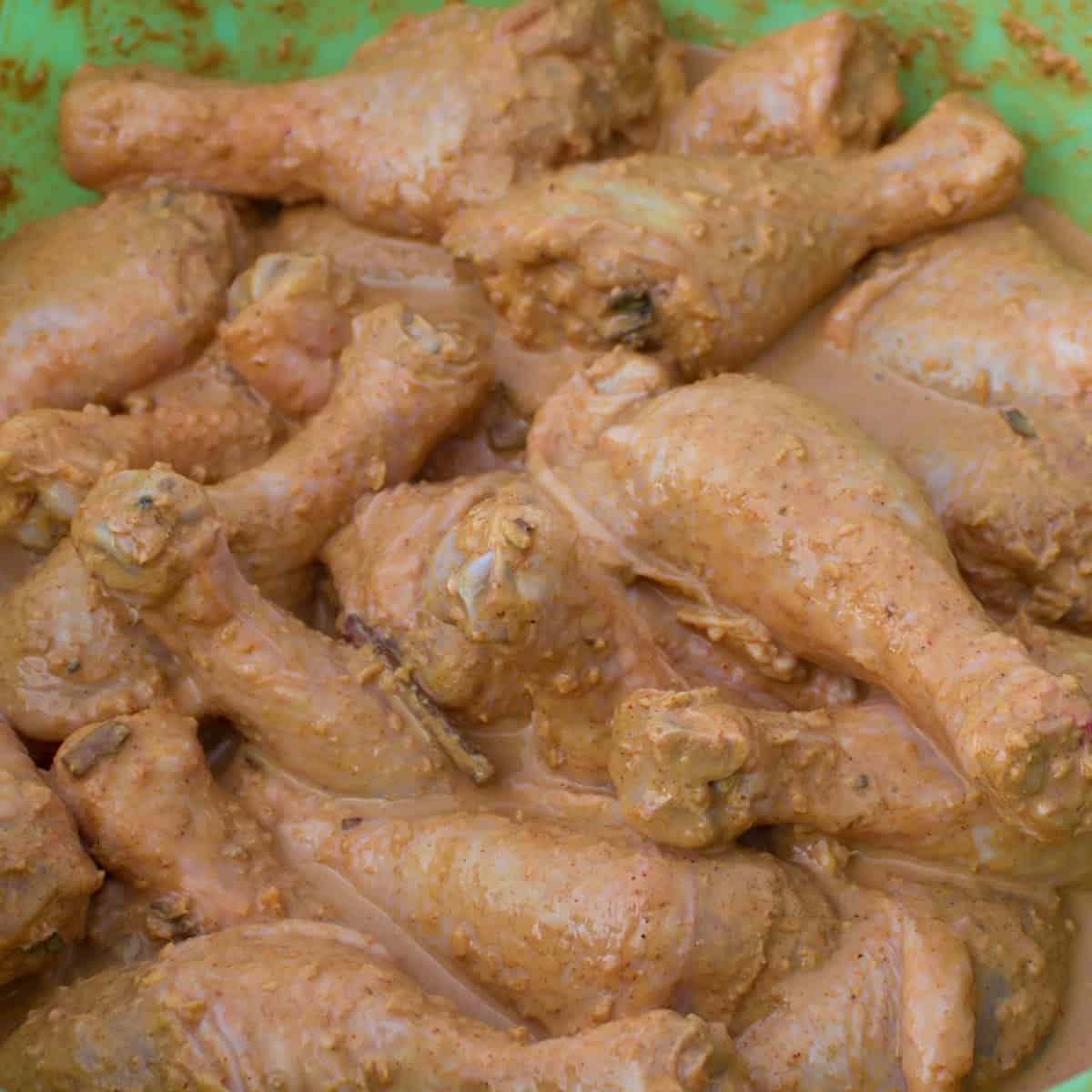 Chicken drumsticks marinating with seasonings in a large bowl.