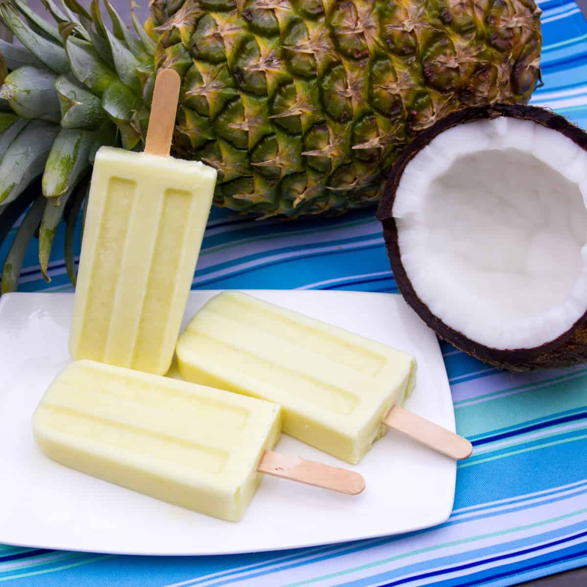 Overhead picture of three popsicles next to a whole pineapple and half of a coconut.