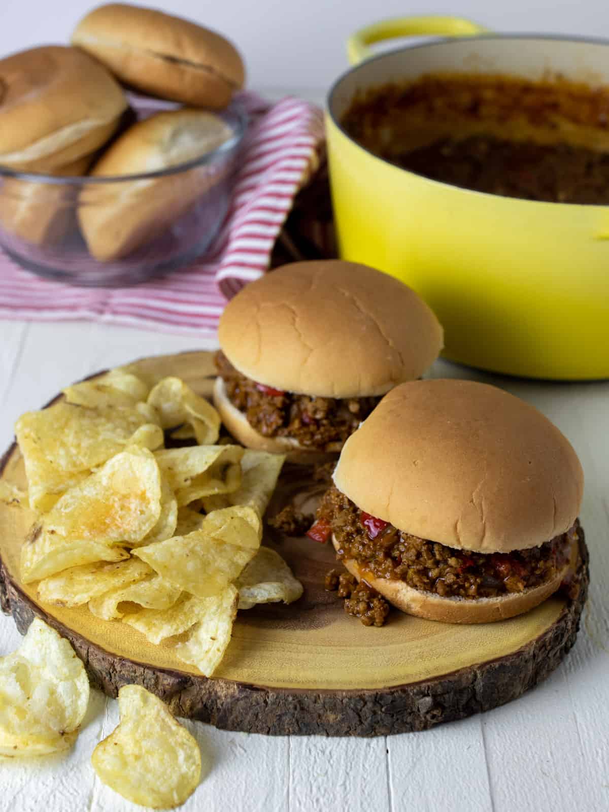 Sandwiches and chips on a round wooden board.