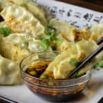 A dumpling being dipped into a small bowl of sauce.