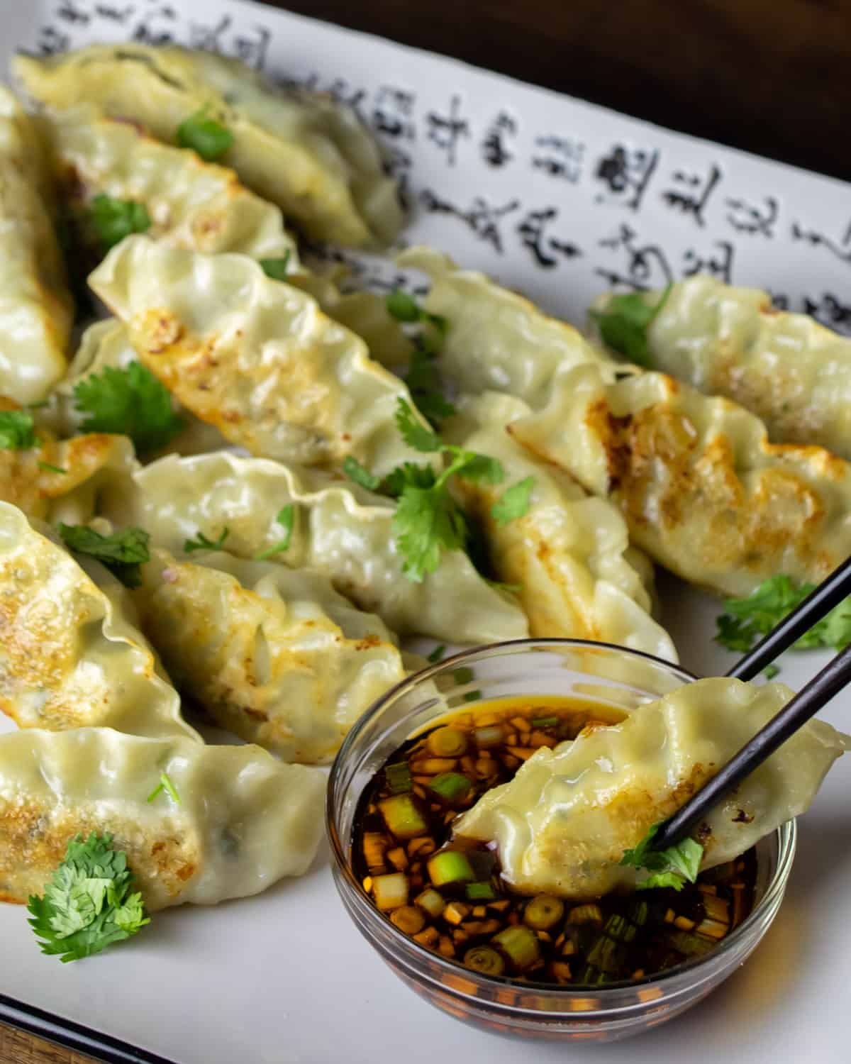 A dumpling held with chop sticks, being dipped in a bowl of sauce.