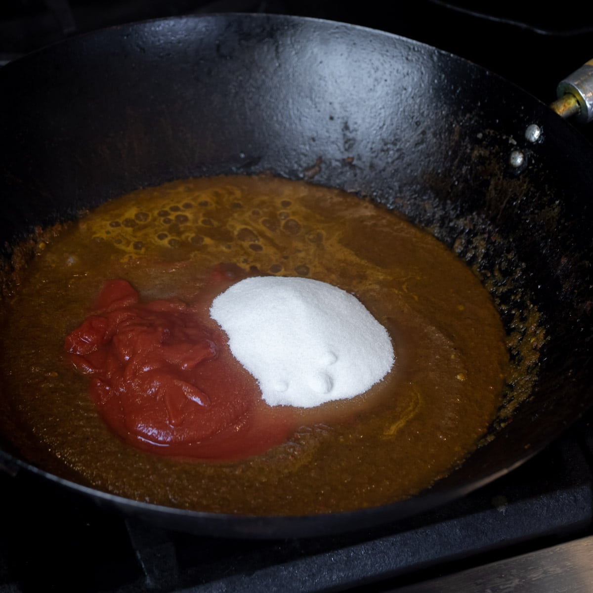 Crushed tomatoes and sugar added to the chili paste in a pan.