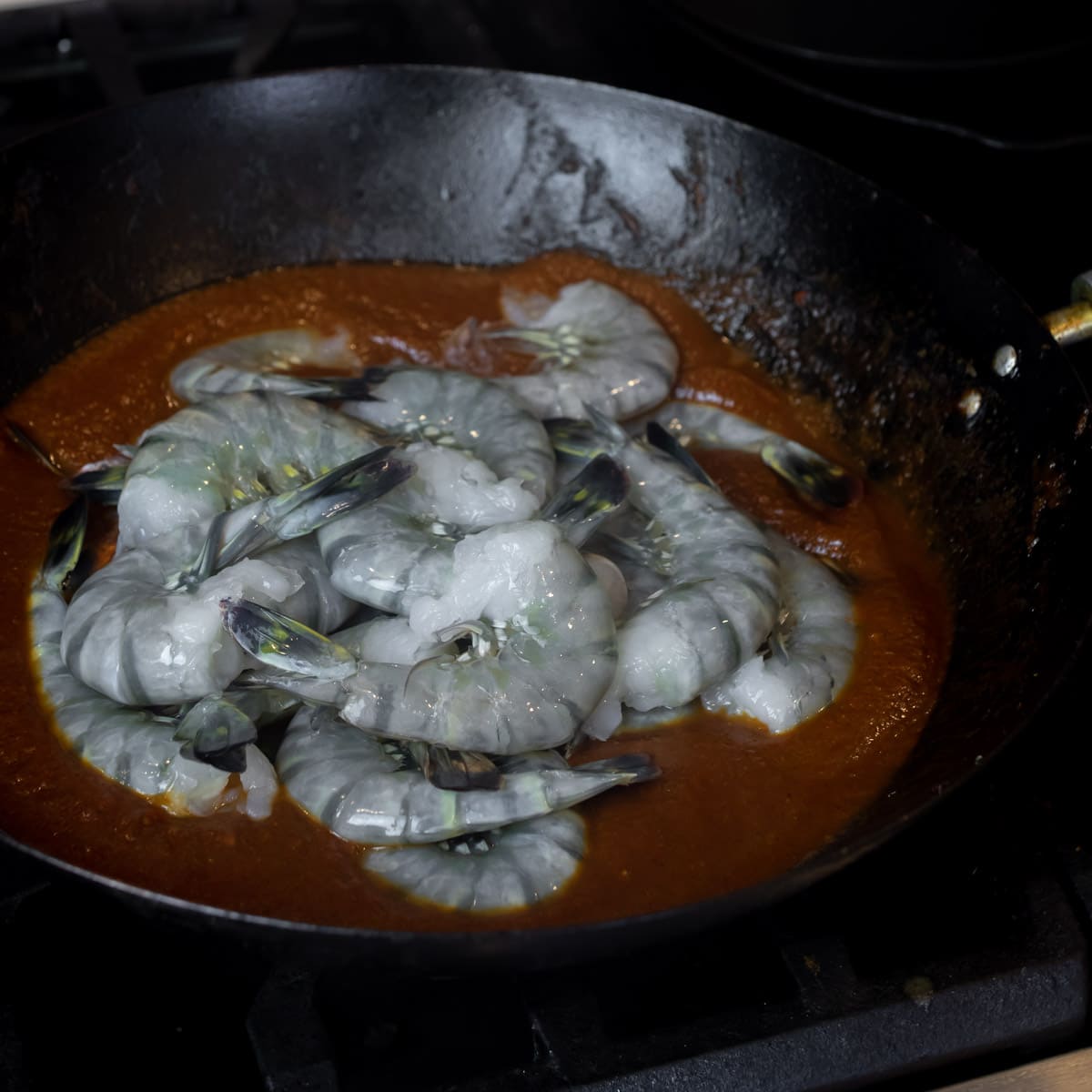 Raw shrimp added to pan on top of simmering sauce.