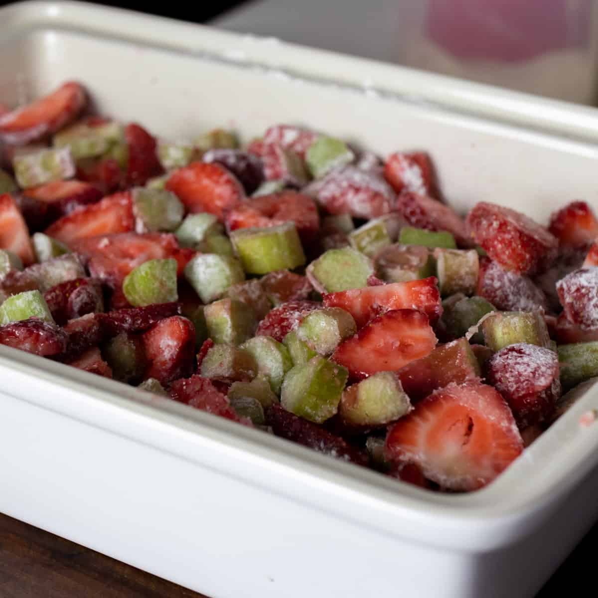 Raw rhubarb and strawberries sliced and mixed with sugar and flour in a baking dish.