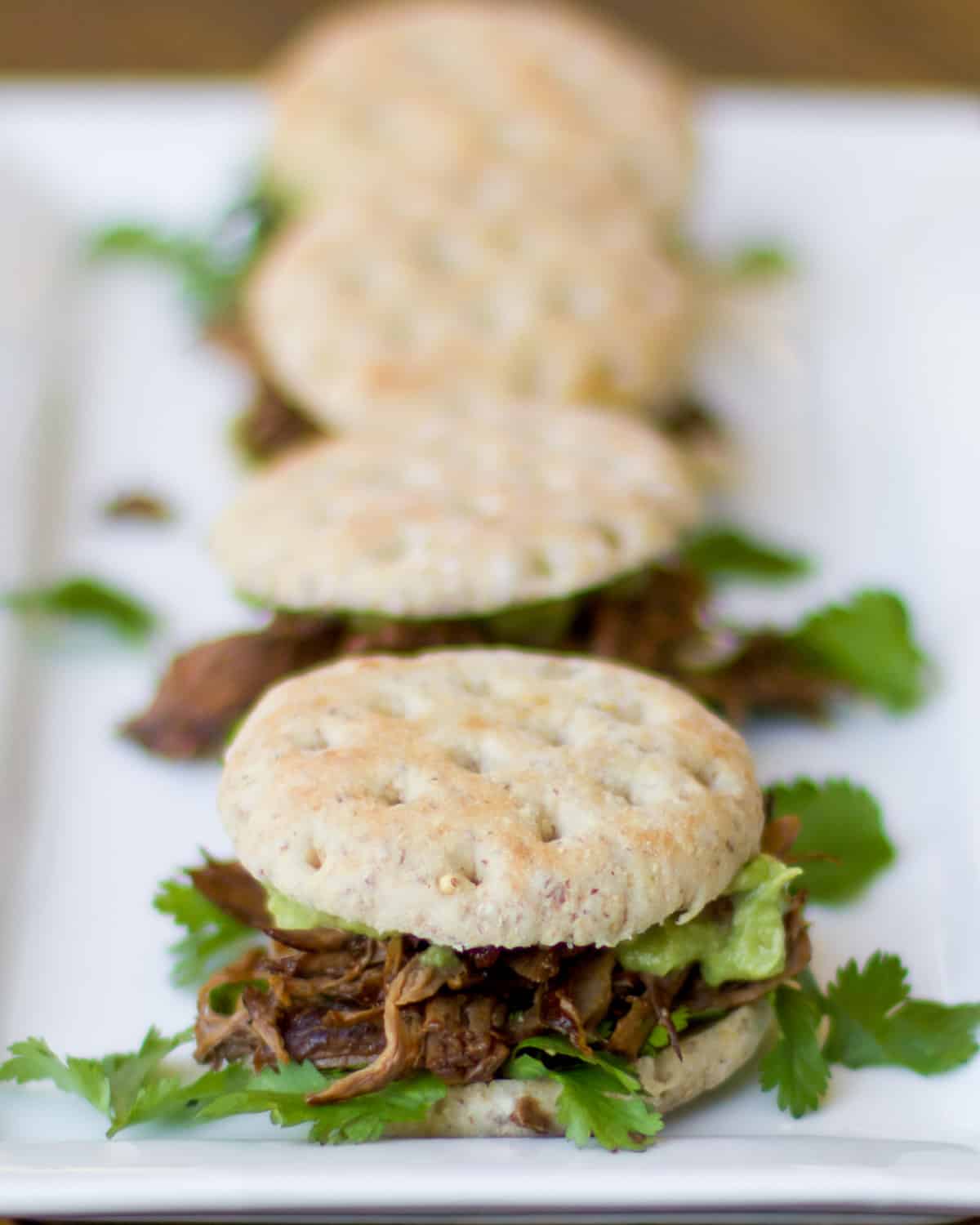 Shredded beef on mini buns on a serving plate.