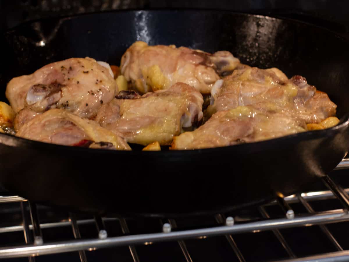 Partially cooked chicken in a cast iron skillet and placed in an oven.