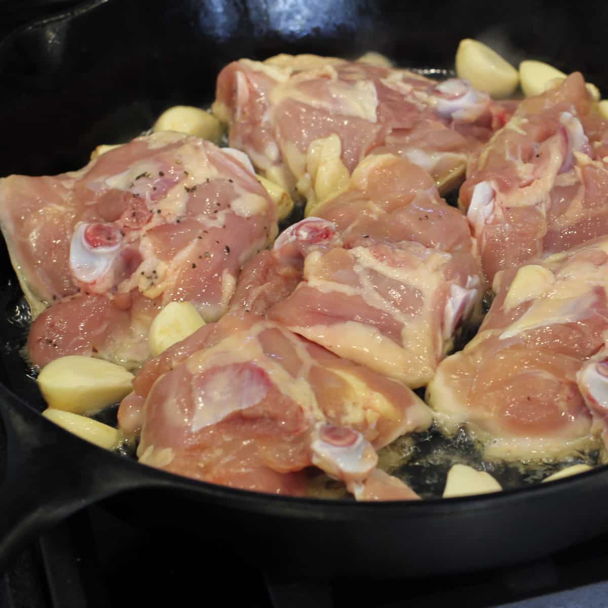 Raw chicken and garlic in a pan.