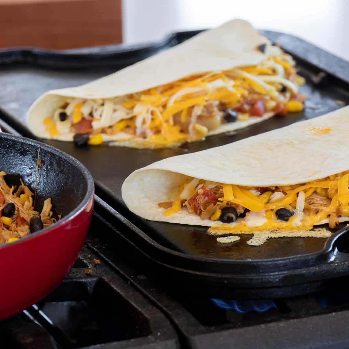 Filling and grated cheese in a soft tortilla shell that is cooking on a griddle.