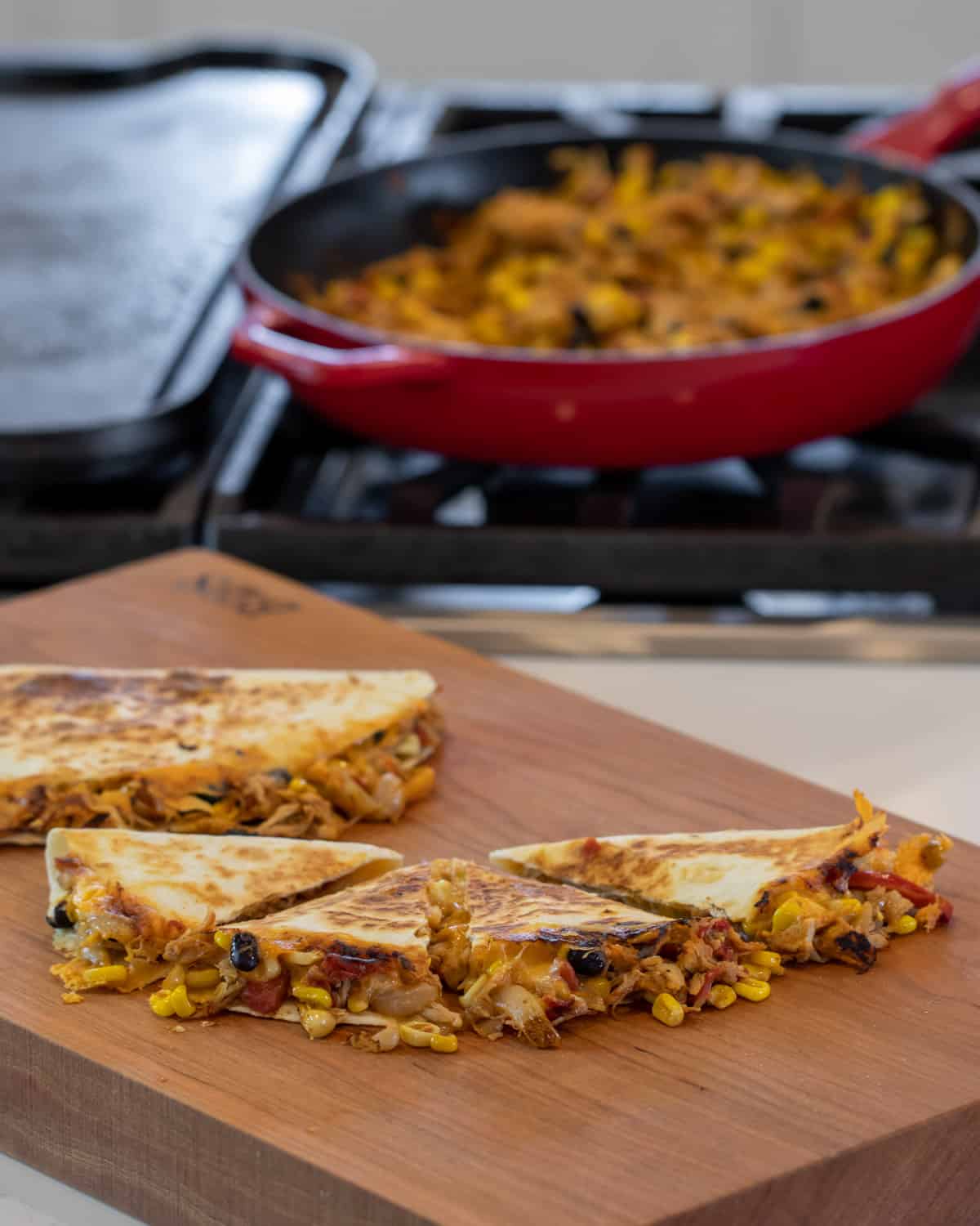 Quesadilla on a cutting board with skillet that has more filling in the background.