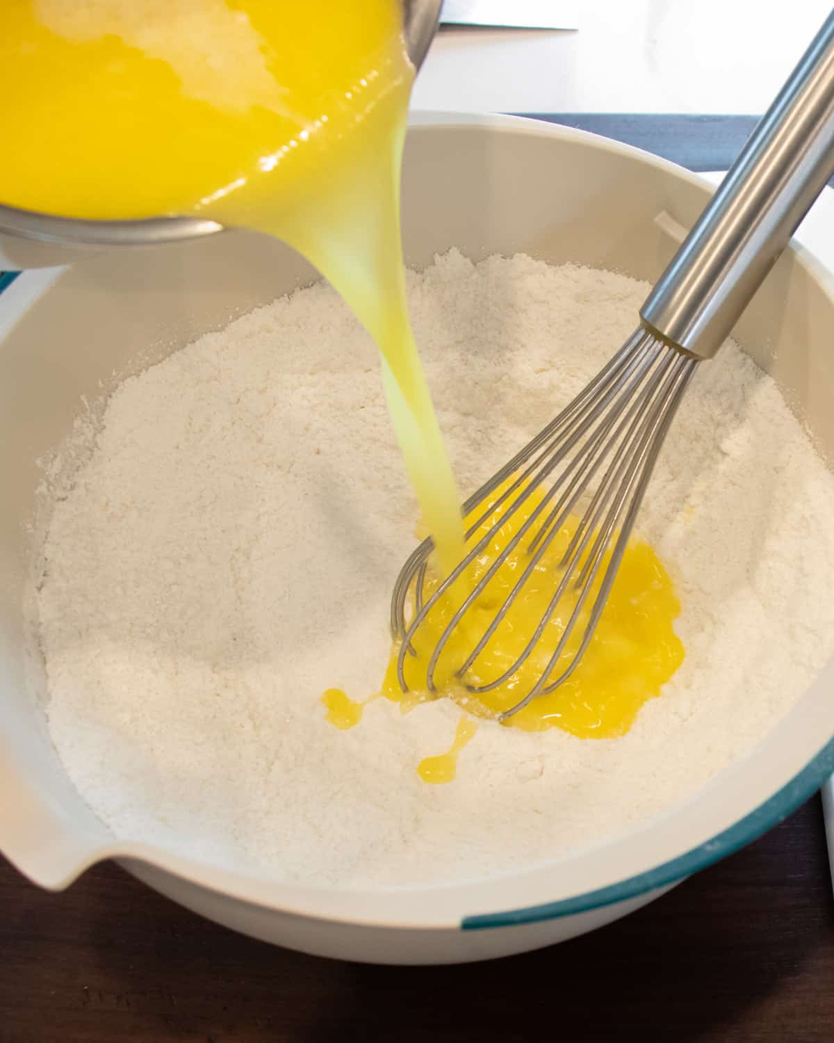 Melted butter being poured into a mixing bowl filled with flour.