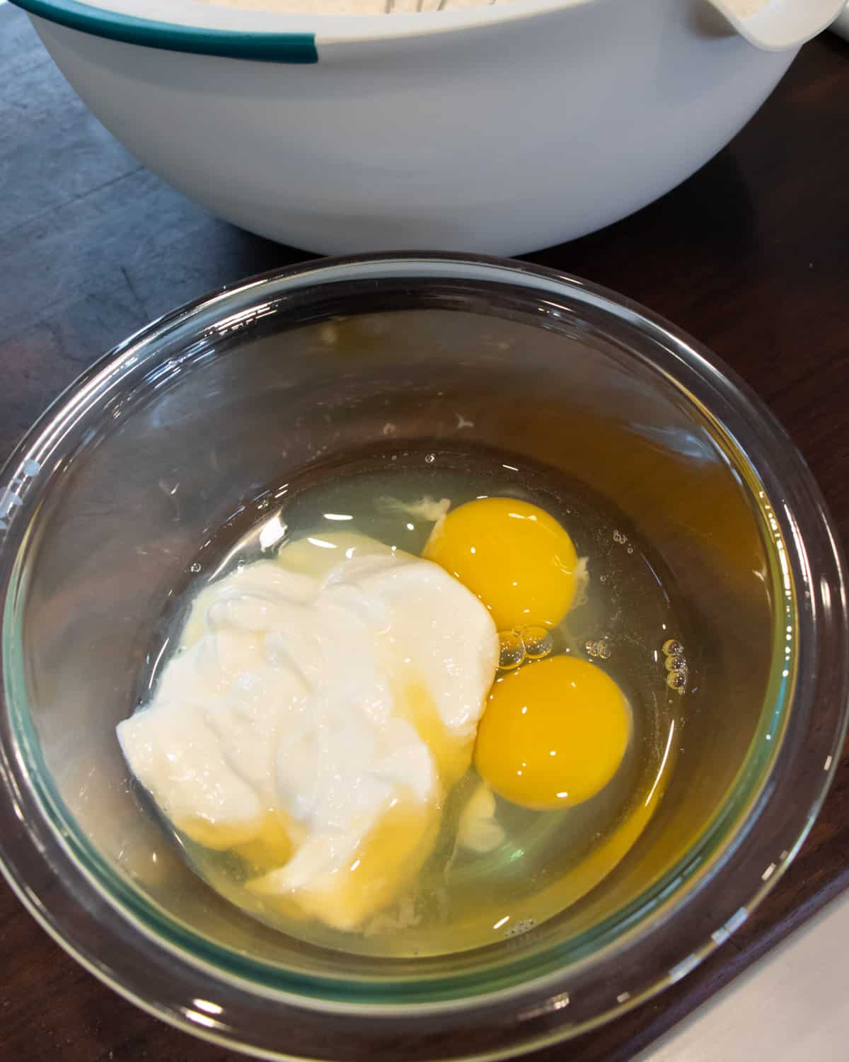 A glass mixing bowl with eggs and sour cream.