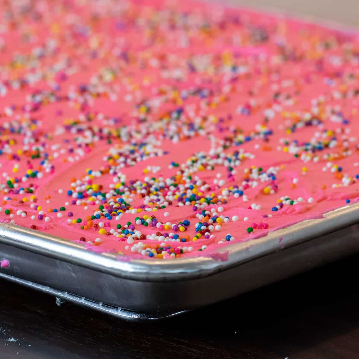 Cake frosted with pink icing with sprinkles all over the cake.