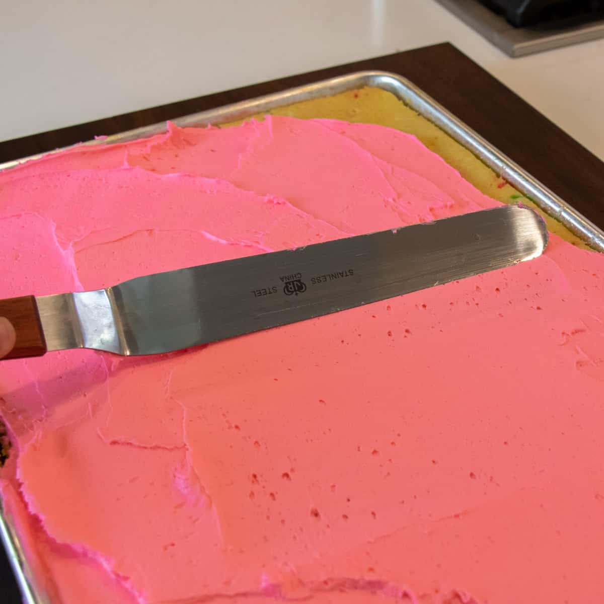 Pink frosting being spread onto a sheet of cake.