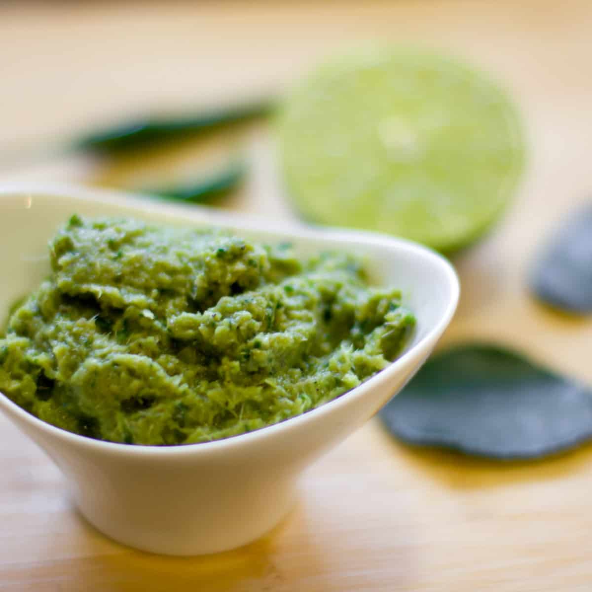 A bowl of curry paste in front of a lime and chili peppers.