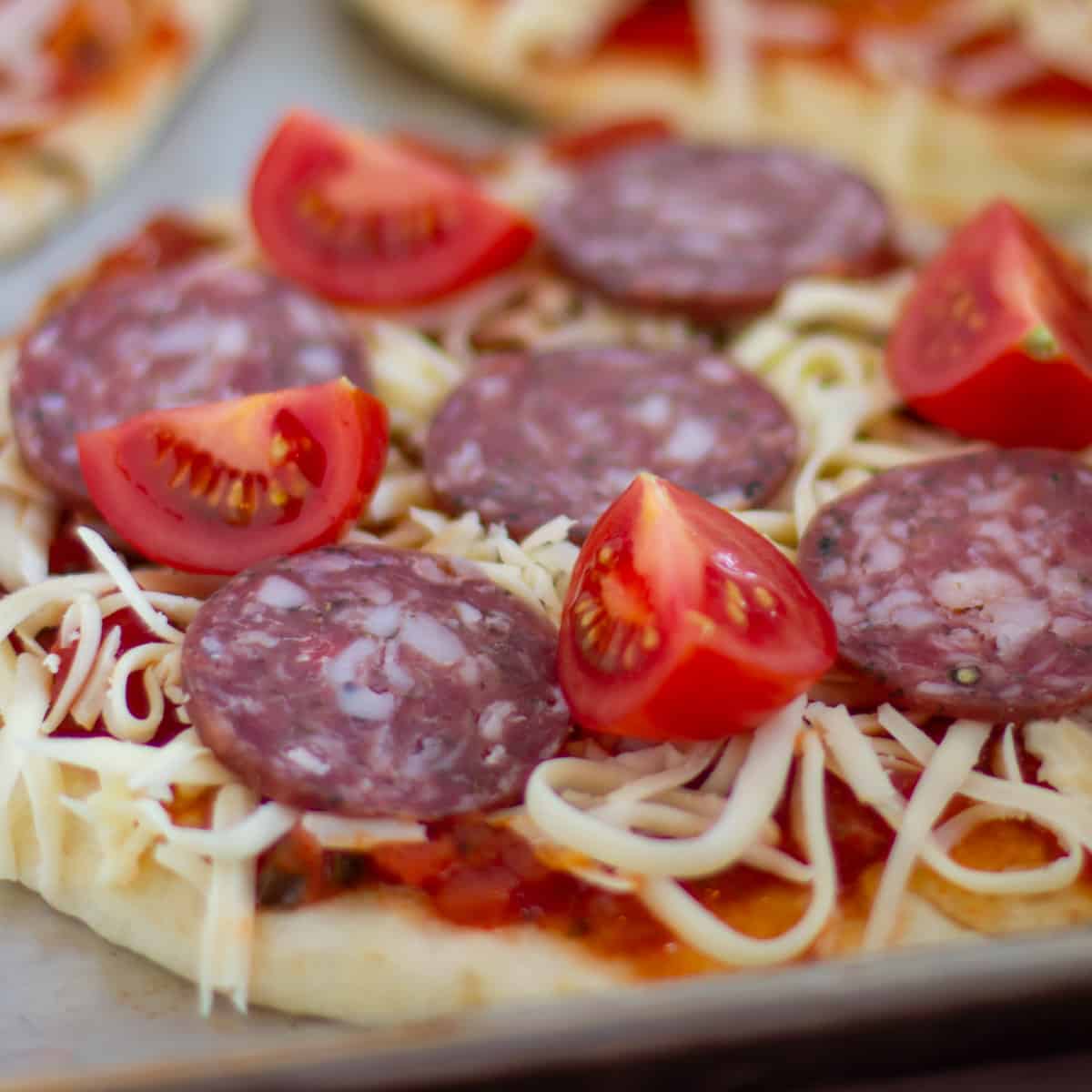 Assembling a pizza with salami and tomatoes.