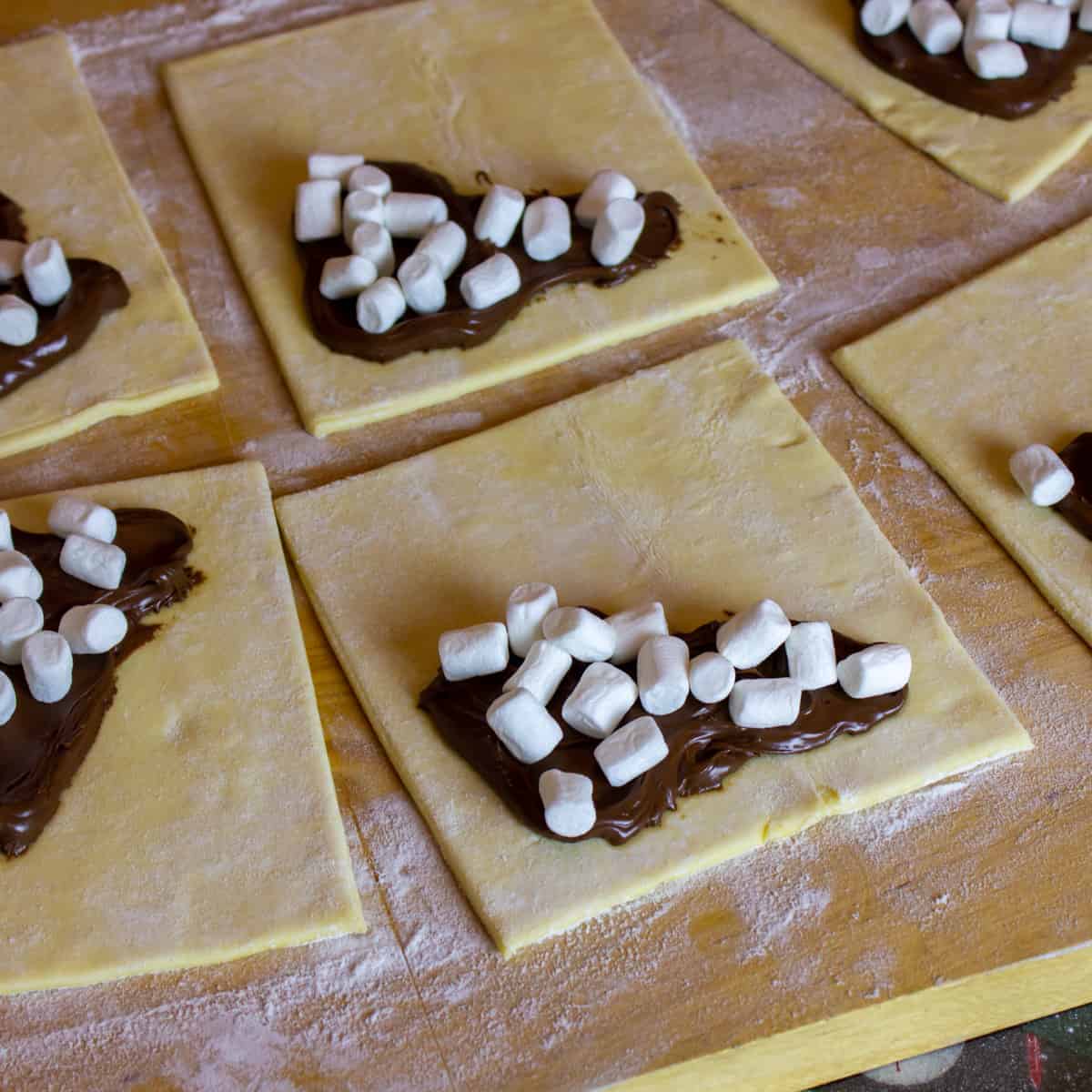 Raw puff pastry squares with a dollop of chocolate spread and some mini marshmallows.