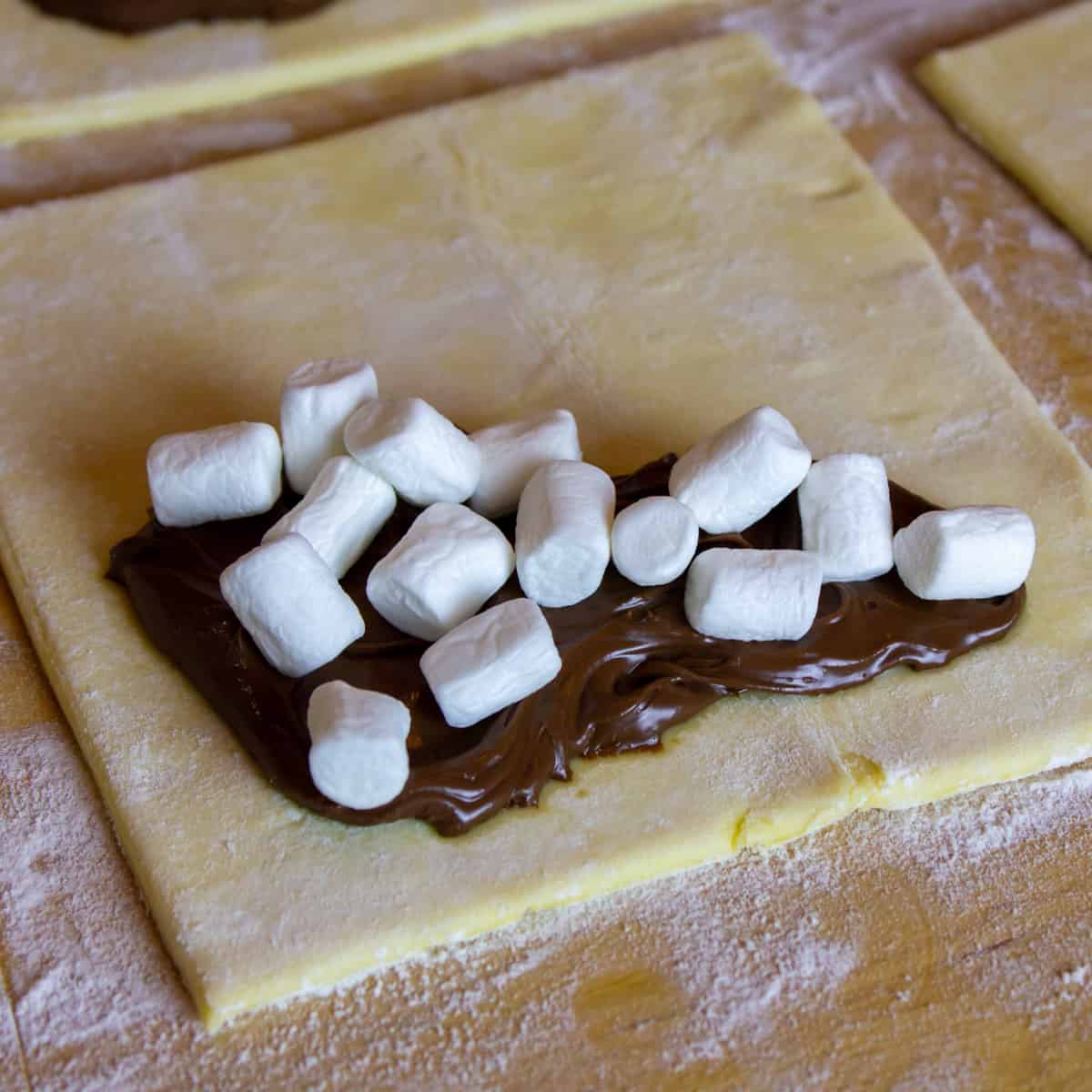 Close up picture of chocolate spread and mini marshmallows on some puff pastry.