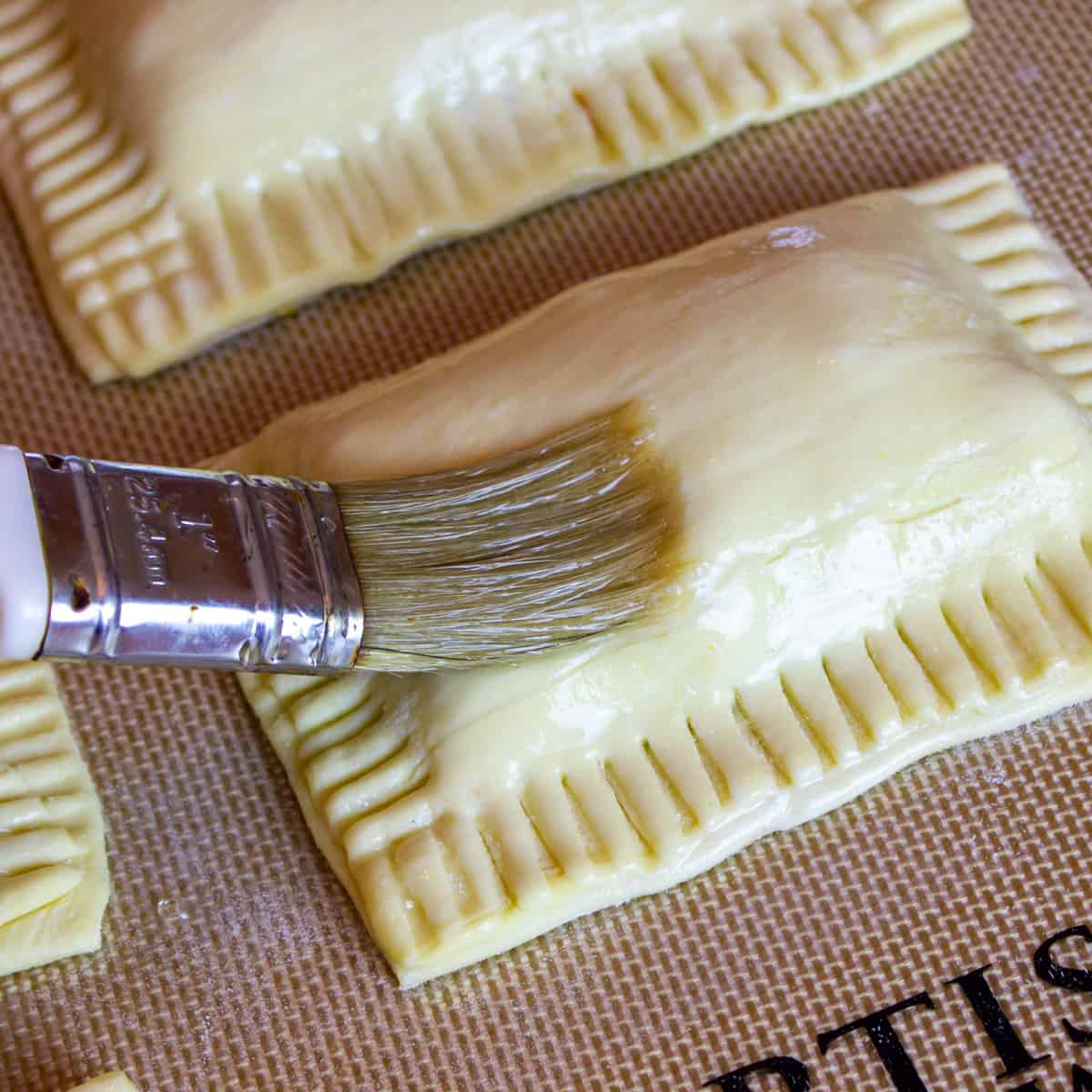Using a pastry brush to add an egg wash to the turnovers.