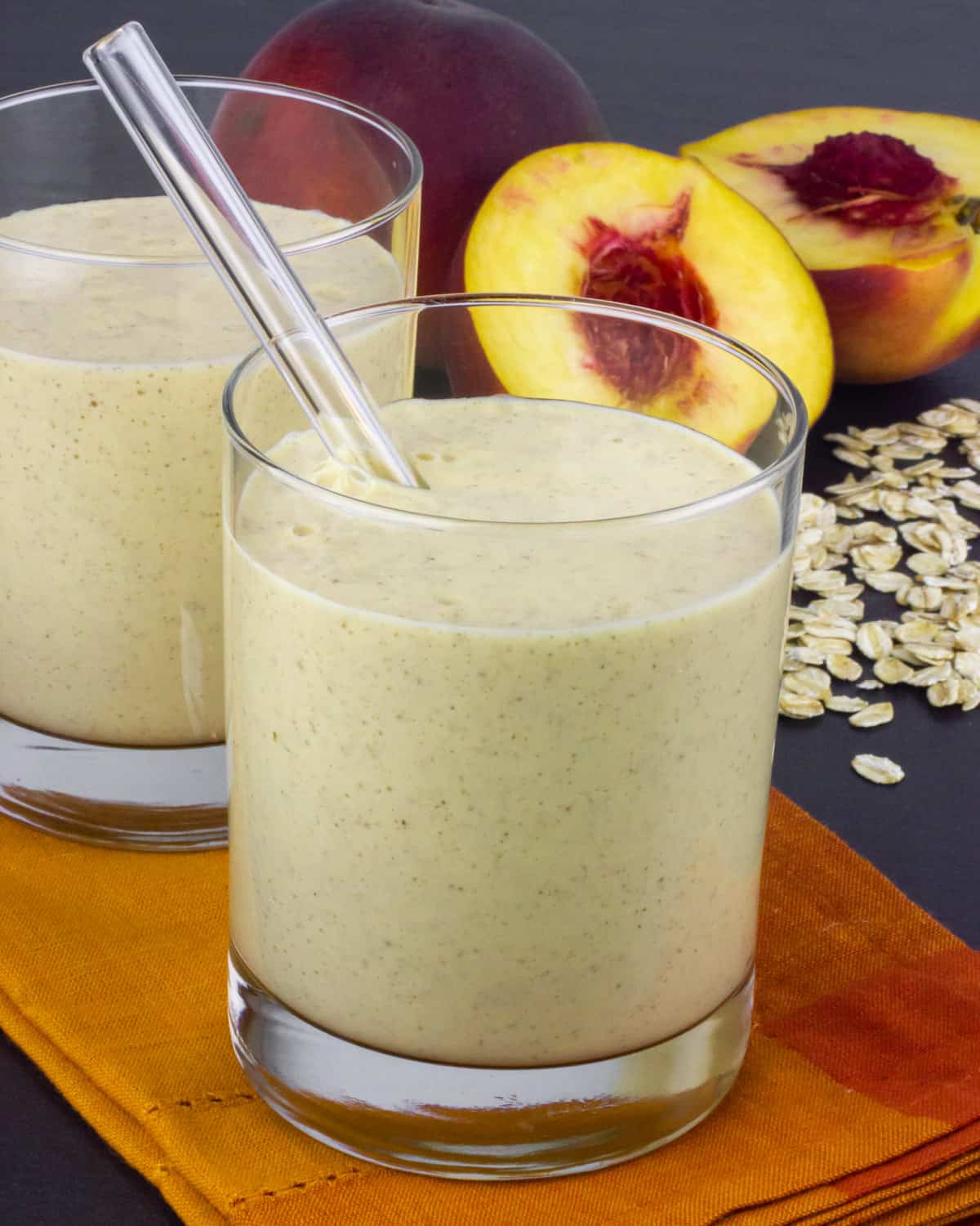 Peaches and a pile of oats behind a glass full of a smoothie.