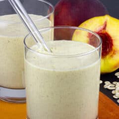 Two glasses of smoothie with halved peaches behind.