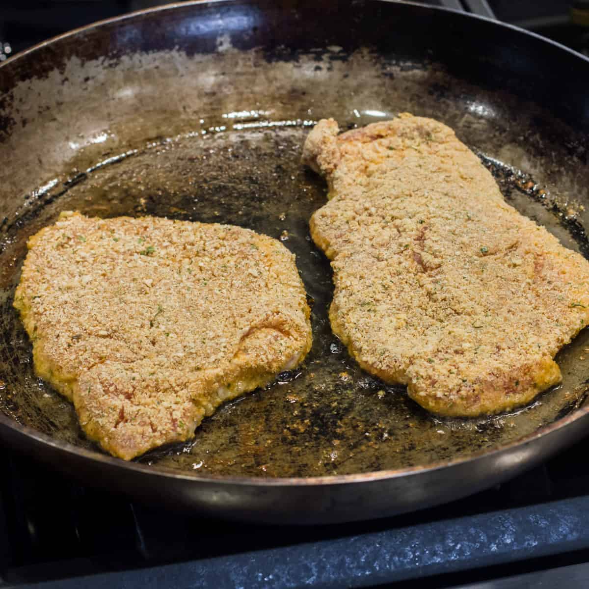 Breaded pork chops in a skillet.