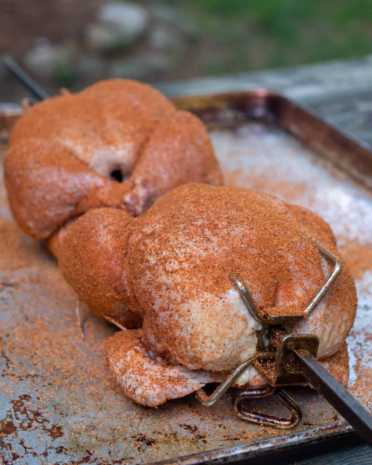 Two whole chickens that have been seasoned with a BBQ rub and put onto a spit.