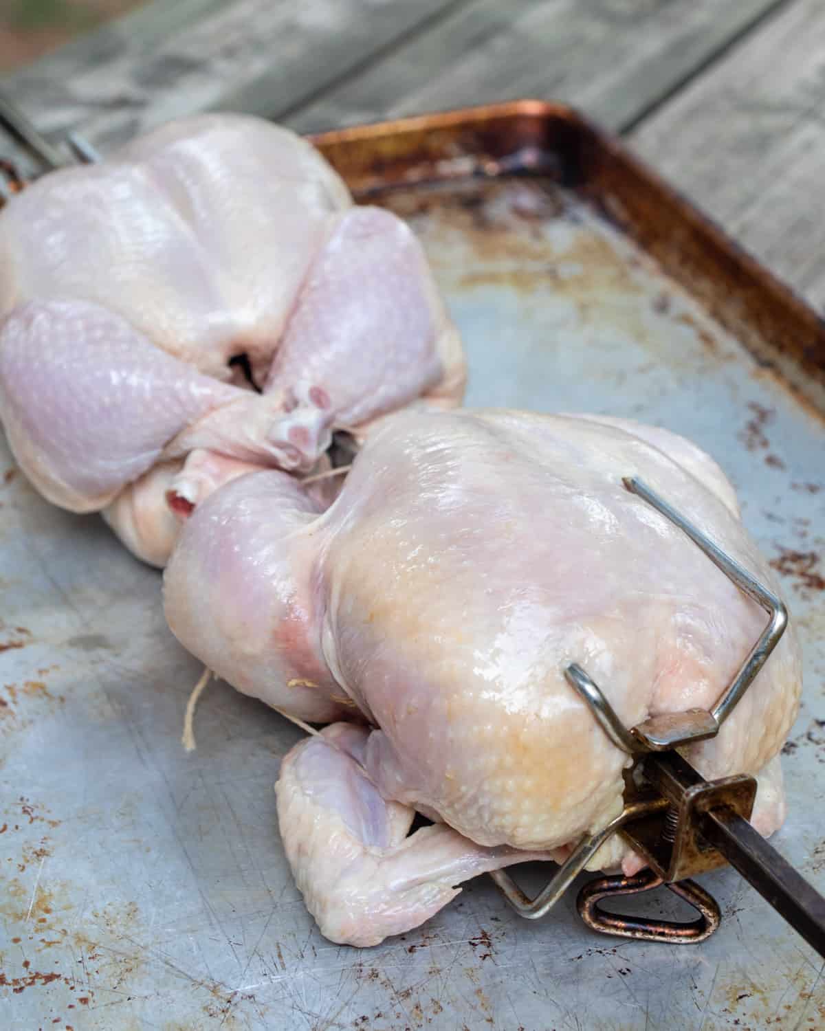 Two raw chickens in a rotisserie spit.