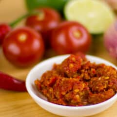 A small bowl of red chili condiment surrounded by various vegetables.