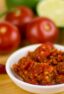 A small bowl of red chili condiment surrounded by various vegetables.