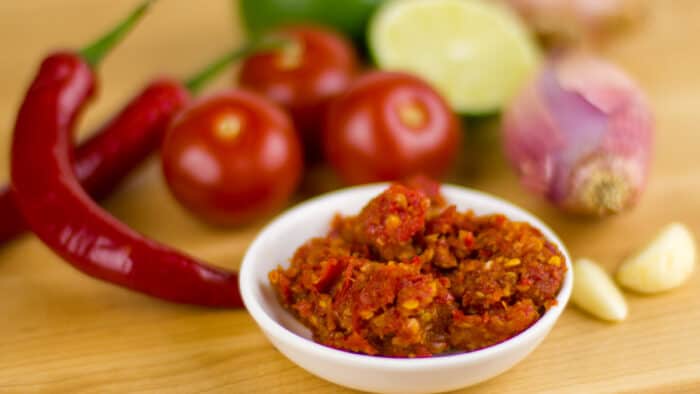 A small bowl of red chili condiment surrounded by various vegetables.