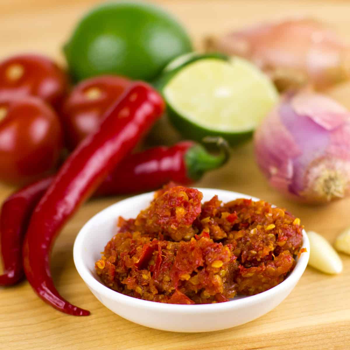 A bowl of chili paste surrounded by vegetables.