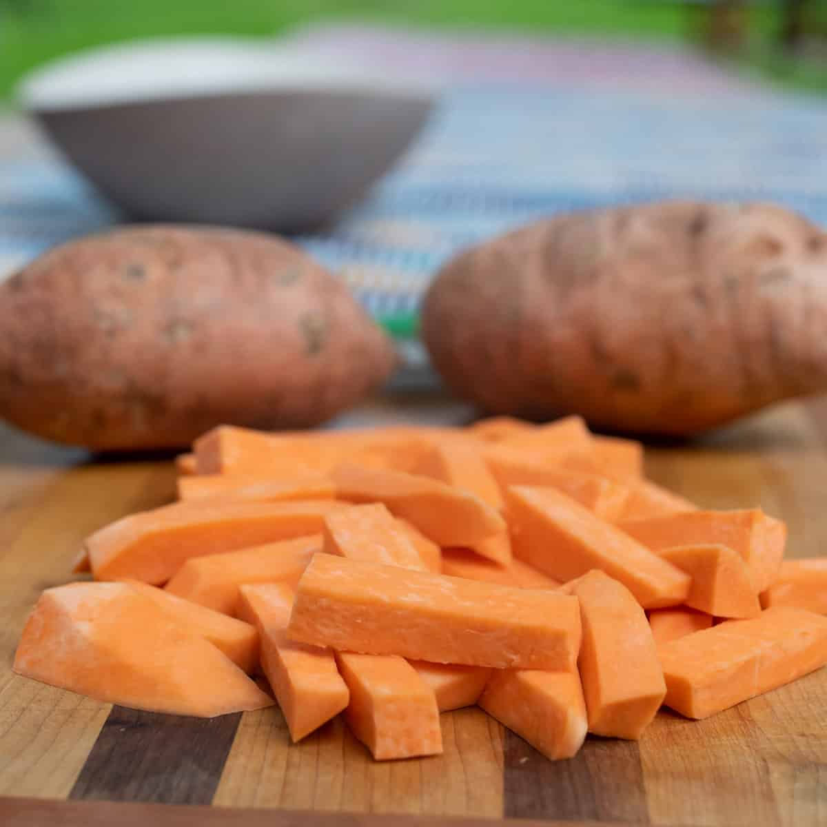 Sweet potato cut in to fat stick shapes with two whole potatoes in the background.