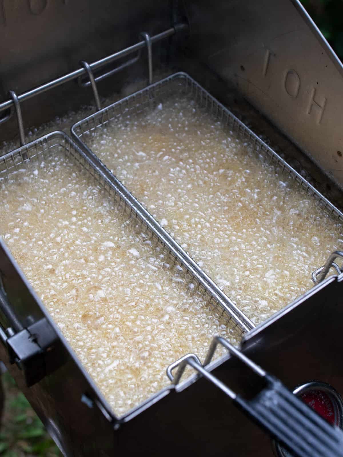 Two fry baskets in the oil with the oil bubbling rapidly.