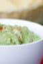 A close up picture of a bowl of mashed avocado.