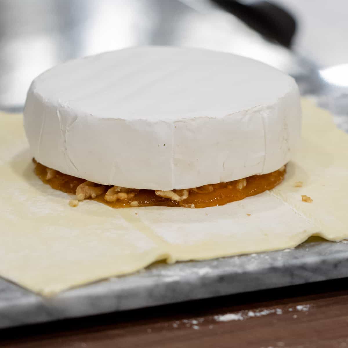 A wheel of brie cheese on top of walnuts and jam.