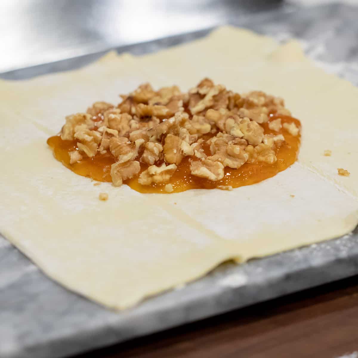 Sheet of raw puff pastry with jam and walnuts.