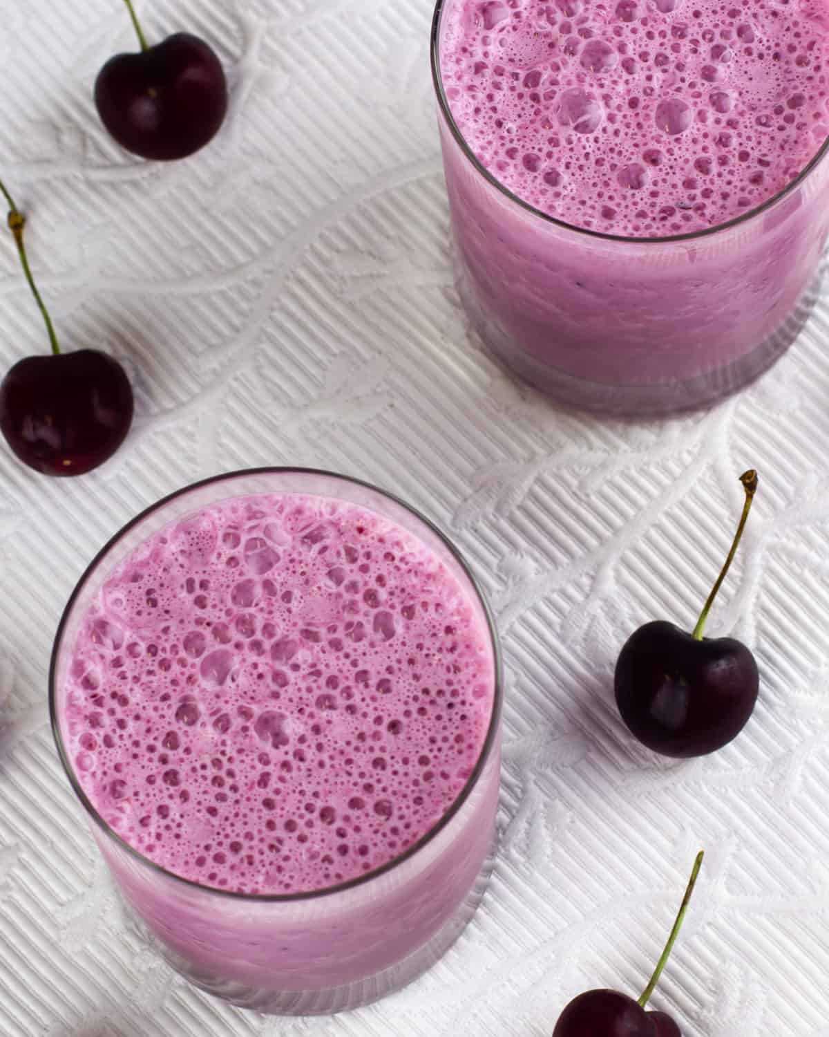 Overhead picture of two glasses full of milkshake surrounded by cherries.