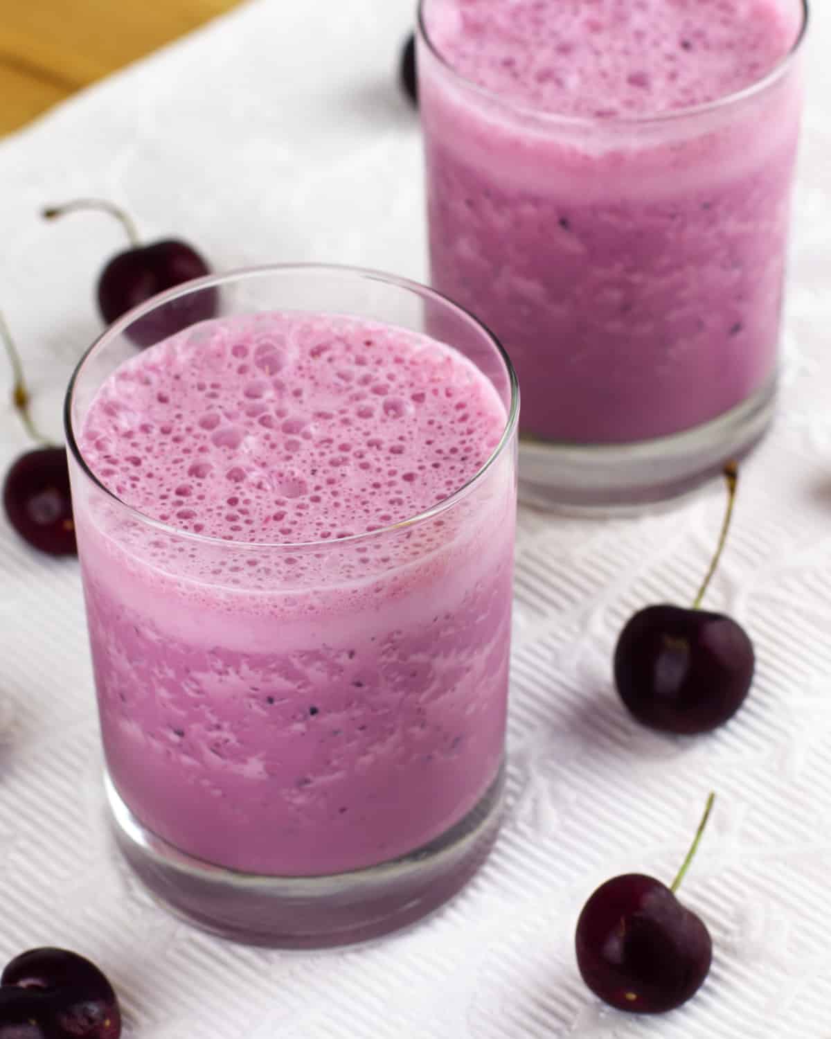 Cherry milkshake in a glass with bubbly froth on top.