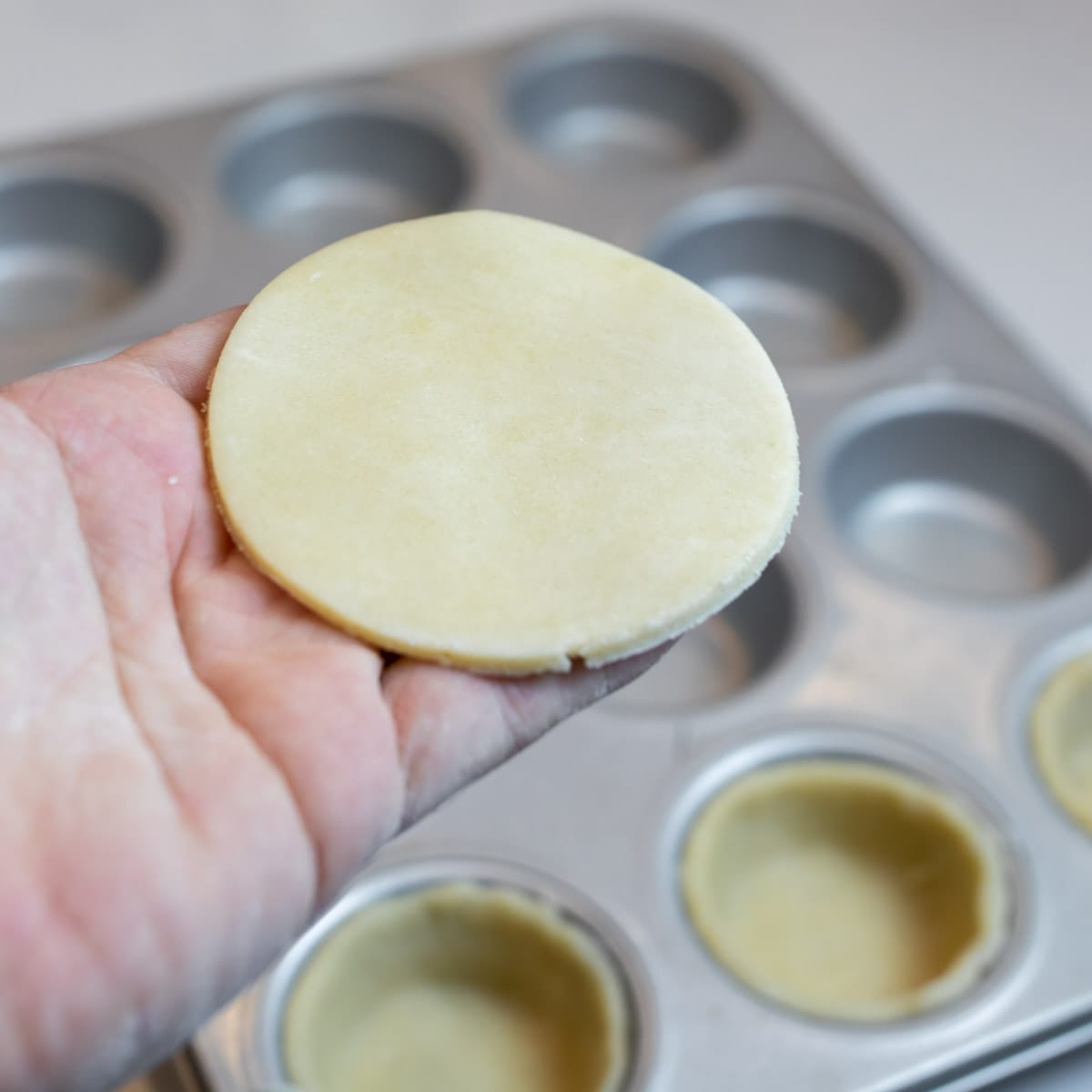 Holding a cut out circle of pastry dough.