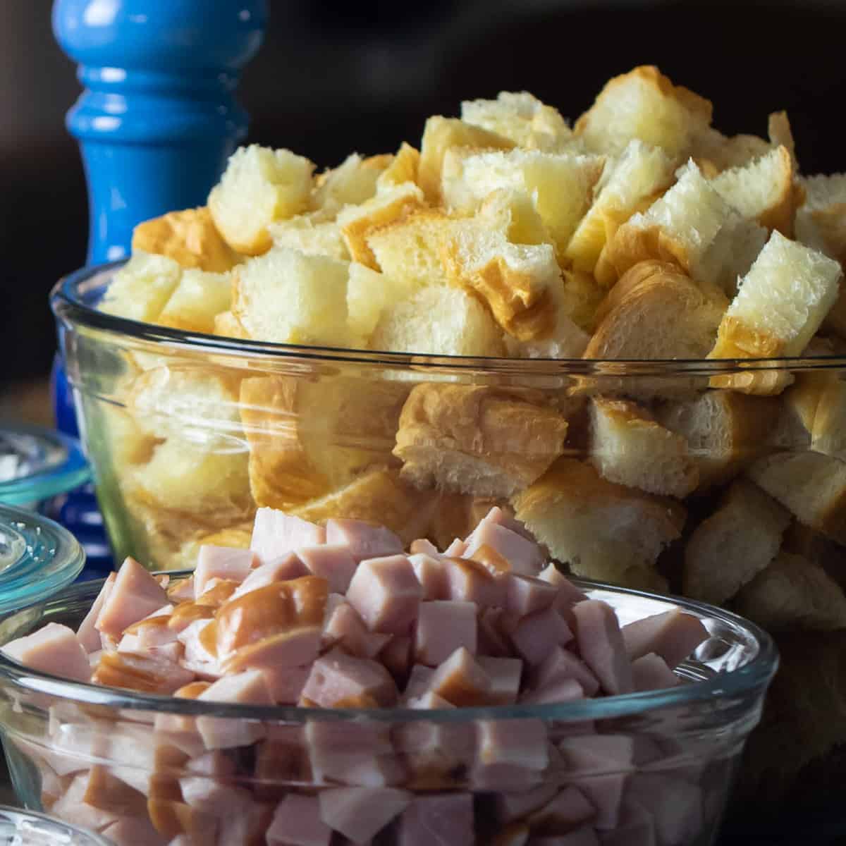 Cubed croissants and ham in glass mixing bowls.