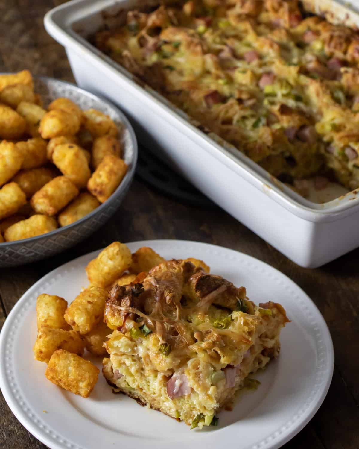 A casserole with eggs, ham and cheese on a plate with tater tots.