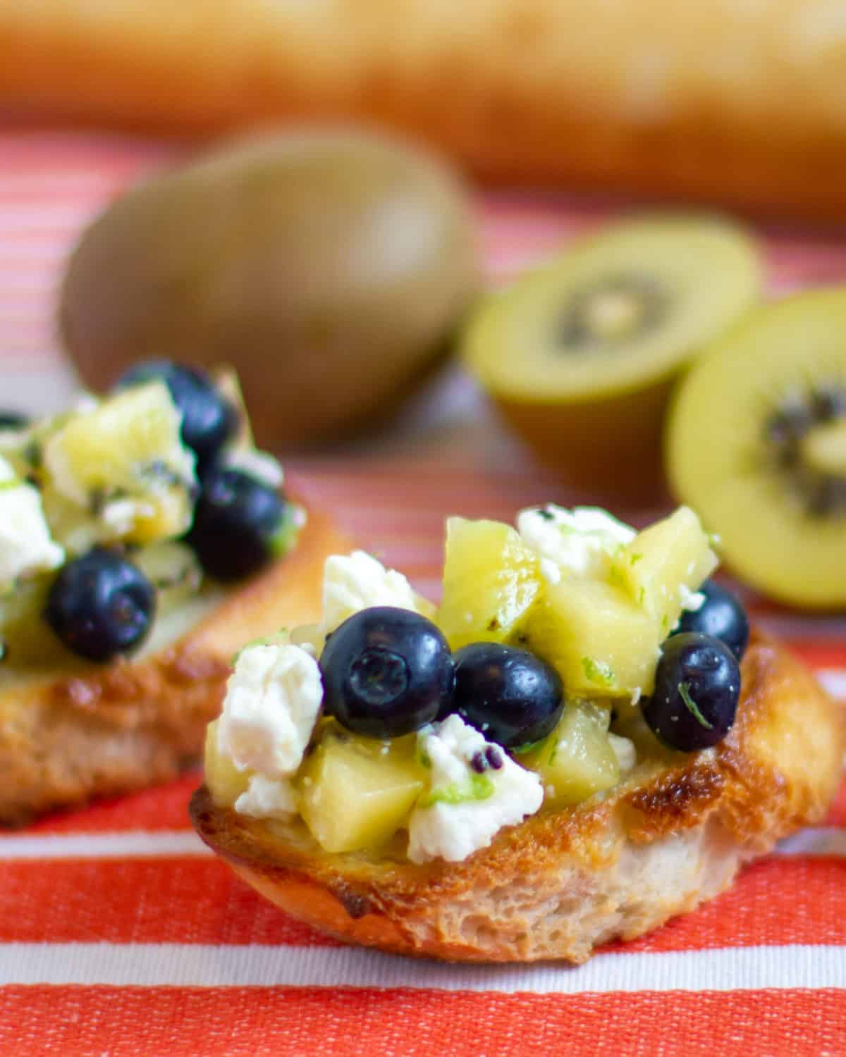 Image of bruschetta with sliced kiwi in the background.
