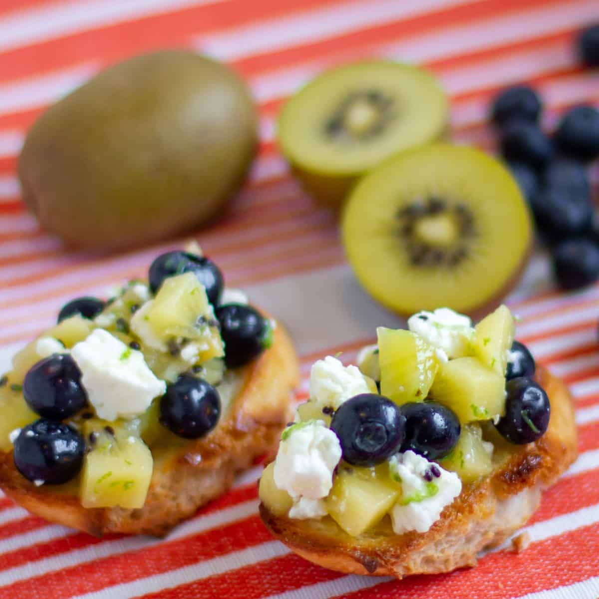 Overhead picture of toasted baguette slices topped with fruit and cheese.