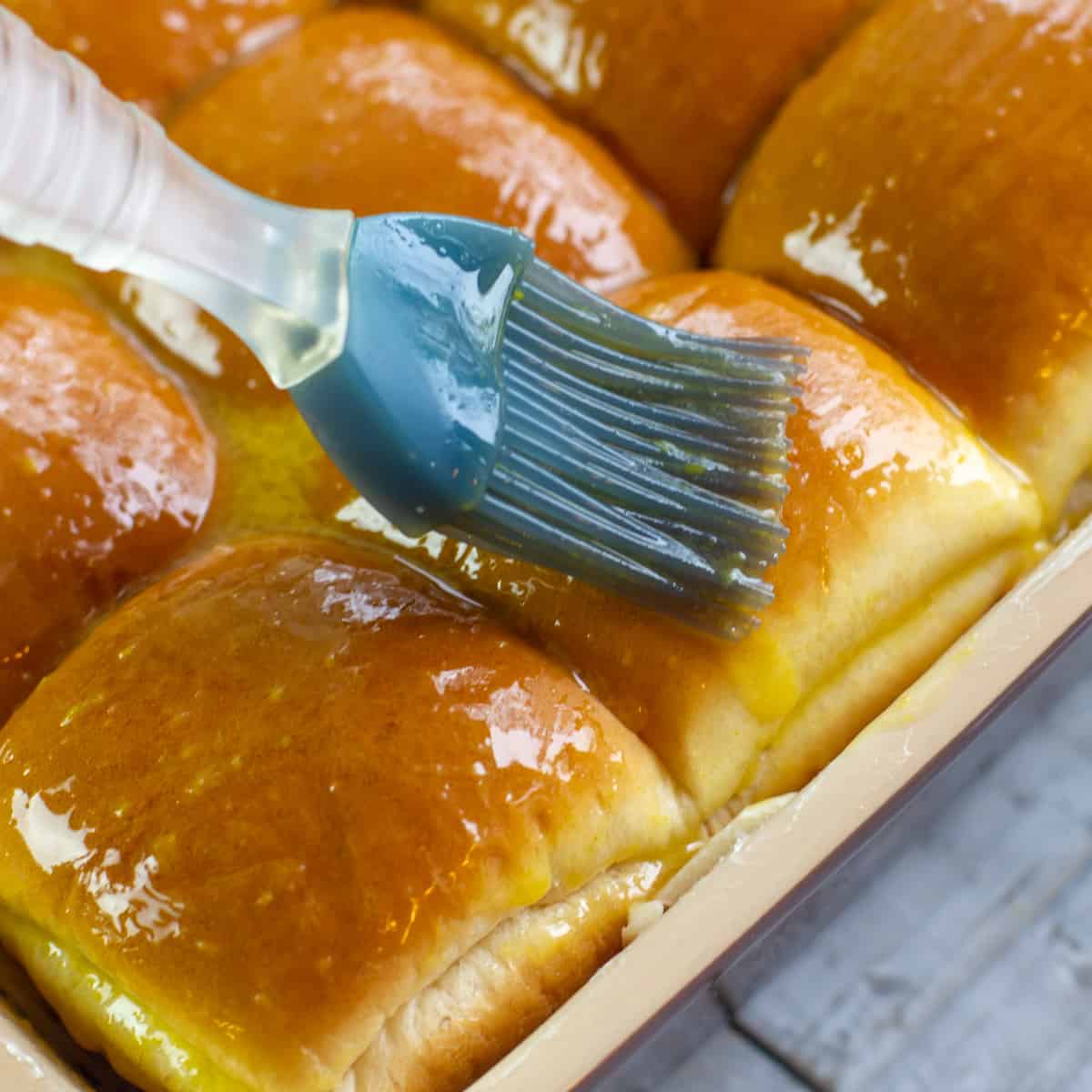 A pastry brush spreading melted butter on slider buns.