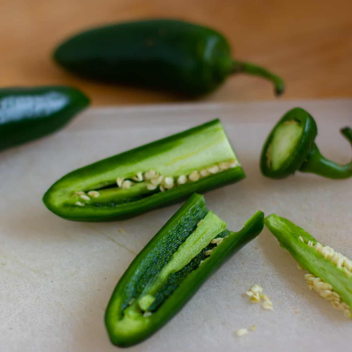 Raw jalapeno peppers halved and cored on a cutting board.
