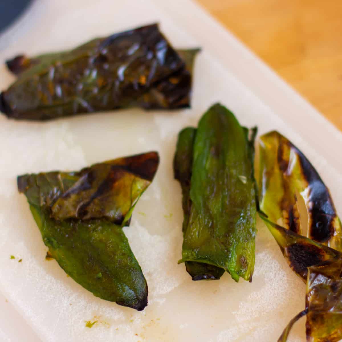 Roasted peppers on a cutting board with the skin being removed.