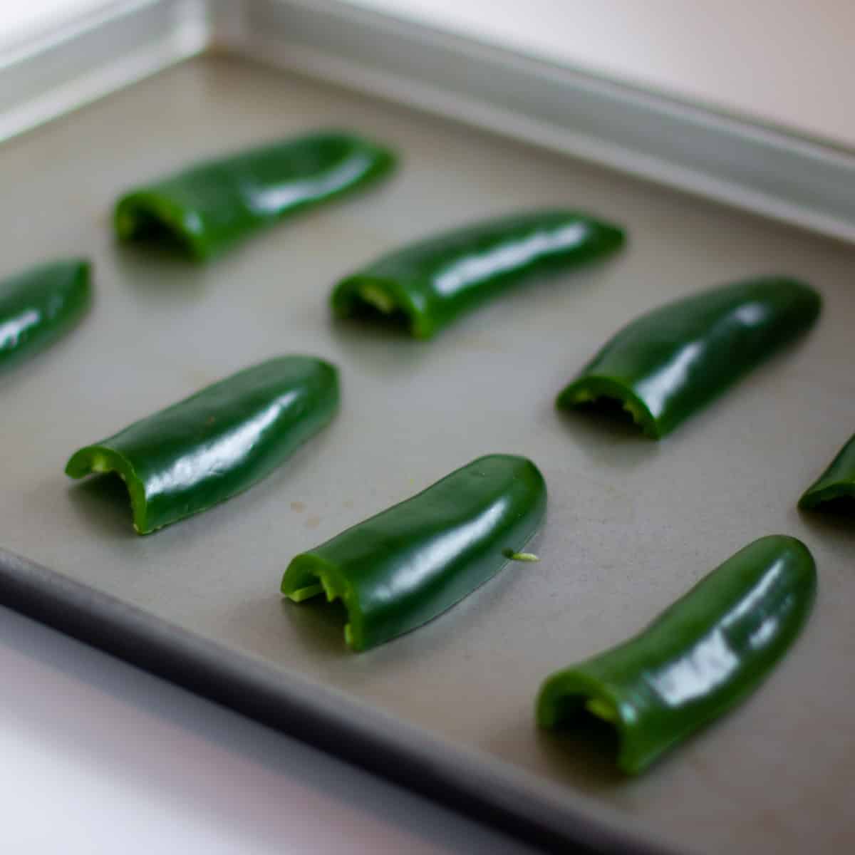 Raw jalapeno peppers on a baking sheet.