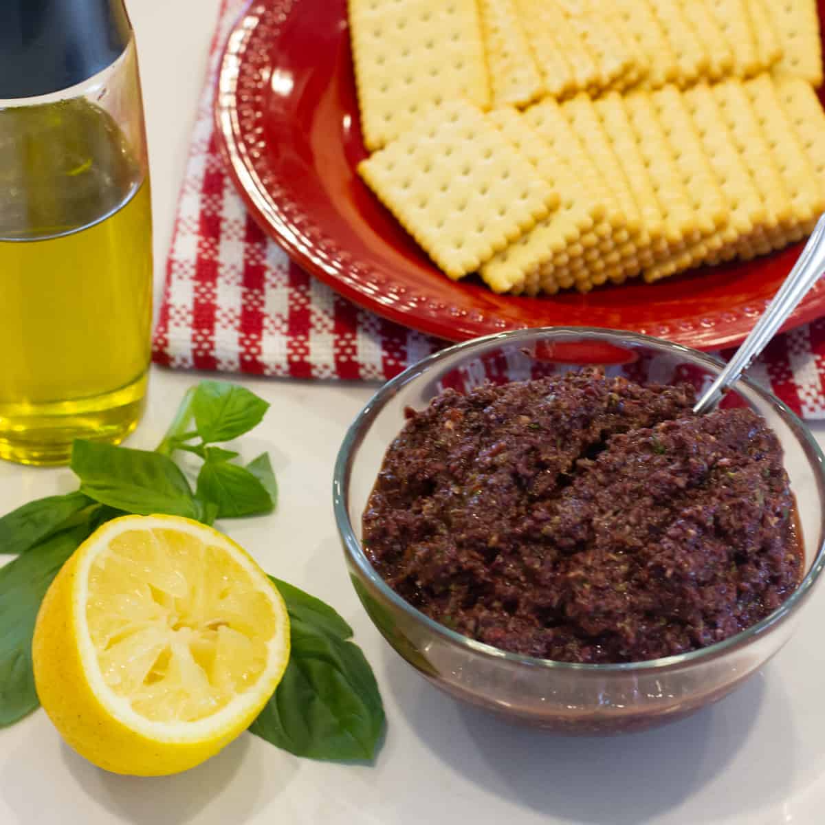 Overheard picture of a bowl of olive spread with a plate of crackers.