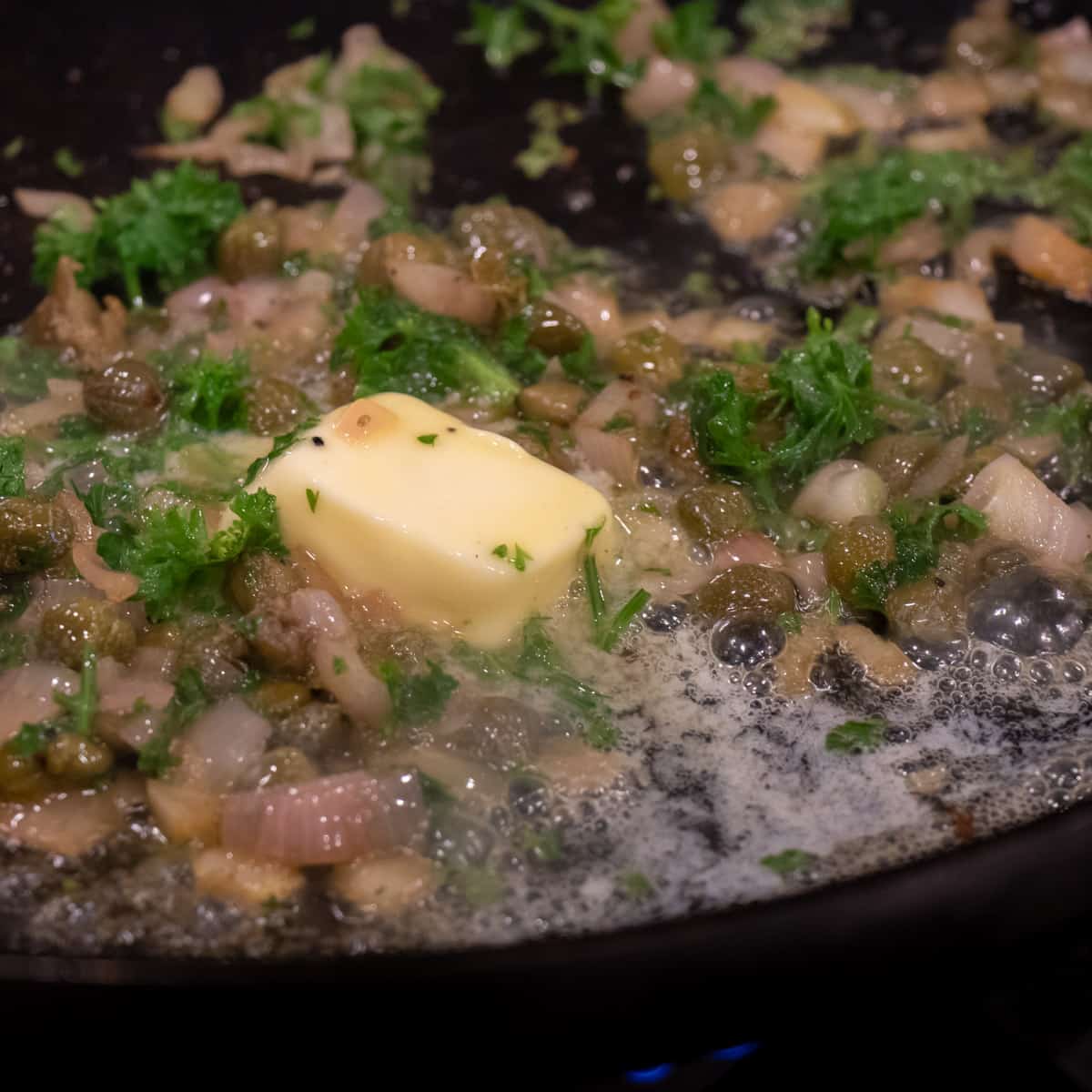 Butter and fresh parsley in a frying pan with shallots and capers.